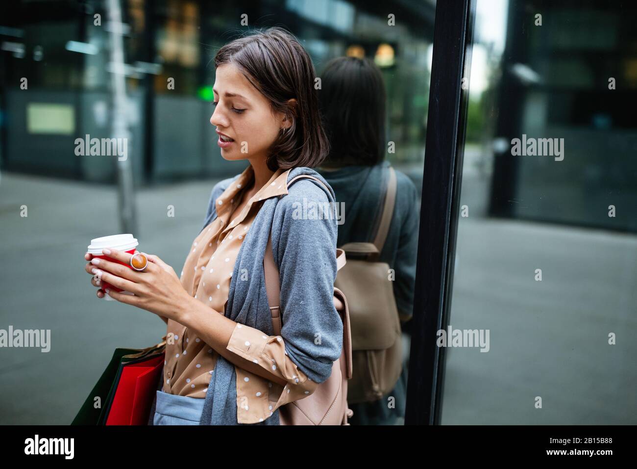 Felice giovane donna bere togliere il caffè e camminare con le borse dopo lo shopping in città. Foto Stock