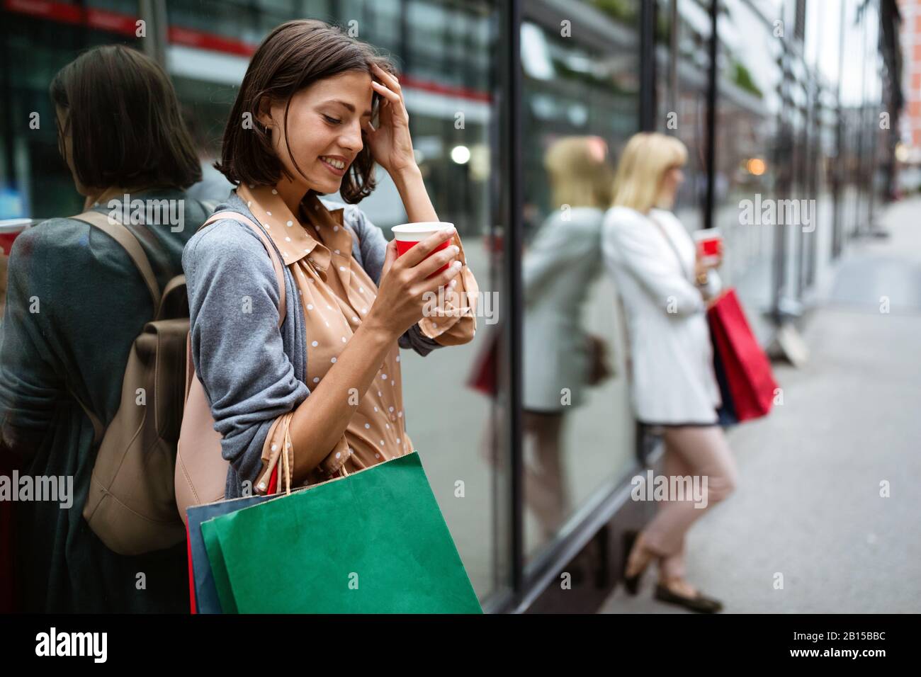 Felice giovane donna bere togliere il caffè e camminare con le borse dopo lo shopping in città. Foto Stock