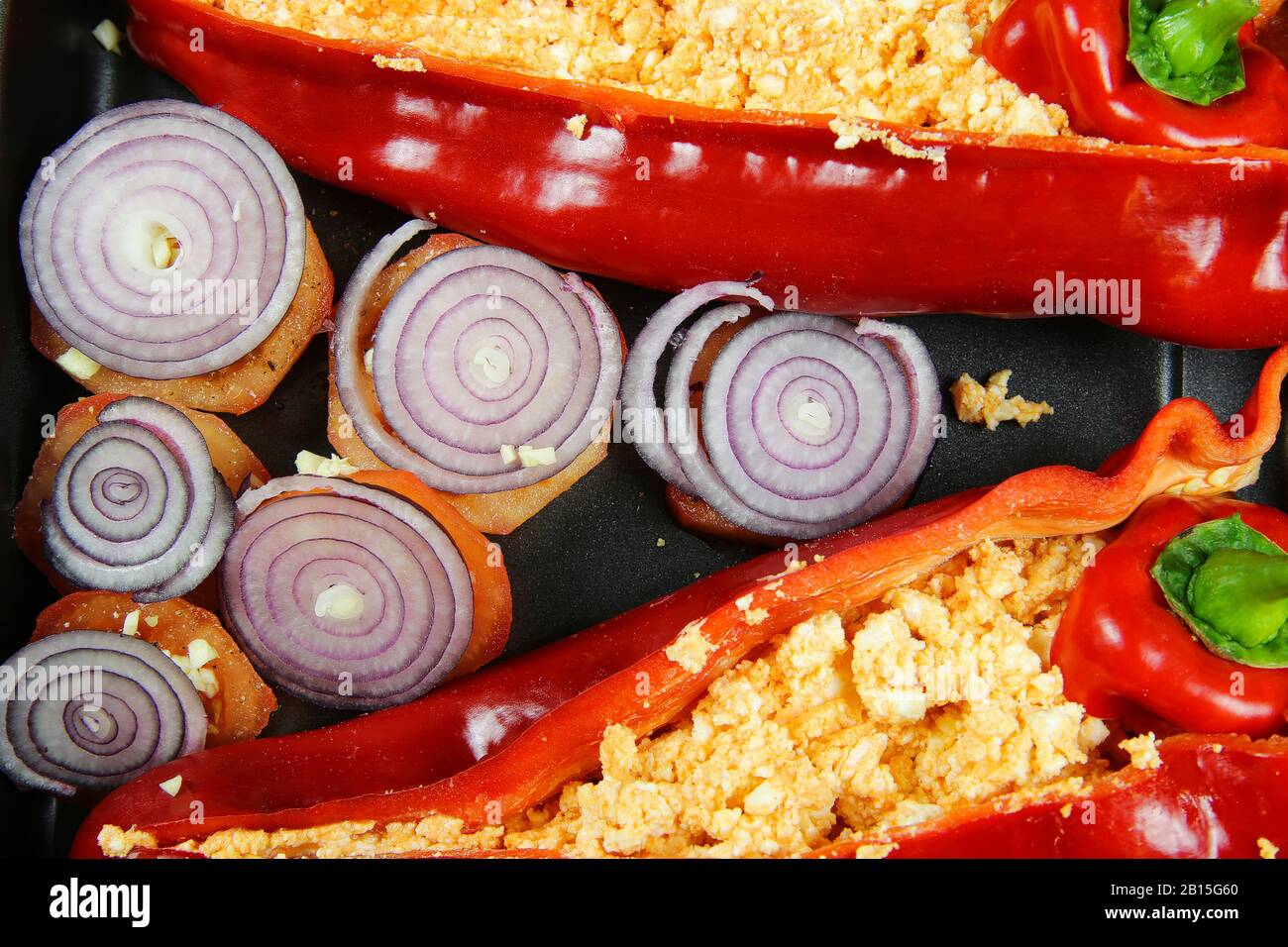 Primo piano di due peperoni rossi cotti al forno riempiti di peperoncino piccante feta e pomodori con anelli di cipolla sul vassoio del forno Foto Stock