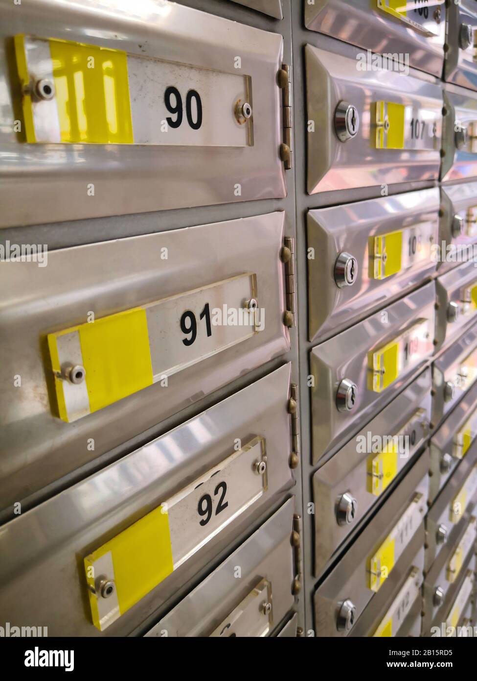 Vista prospettica di scatole di posta in acciaio grigio con etichette gialle e numeri neri. Ufficio postale a Siviglia, Spagna Foto Stock