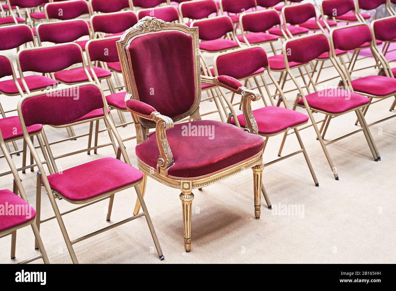 Trono unico o poltrona cerimoniale con seduta in velluto e dettagli dorati tra tante semplici sedie simili. Unicità o concetto di esclusività Foto Stock