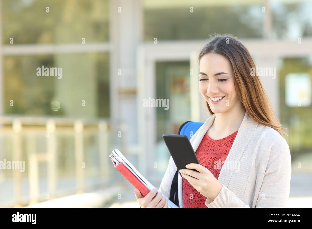 Felice studente che usa il telefono cellulare a piedi in un college Foto Stock