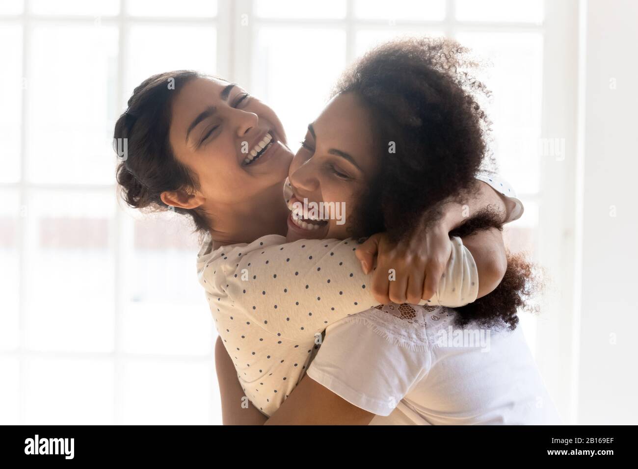 Amici di etnia indiana e africana felici si coccolano l'un l'altro all'interno Foto Stock