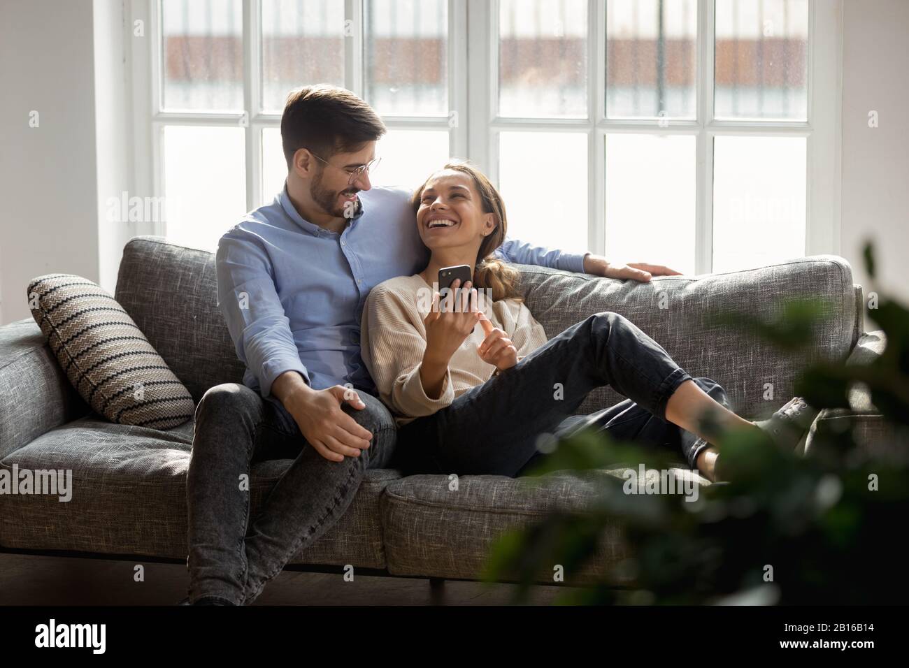 Coppia millenaria innamorata seduto sul divano di parlare con lo smartphone Foto Stock