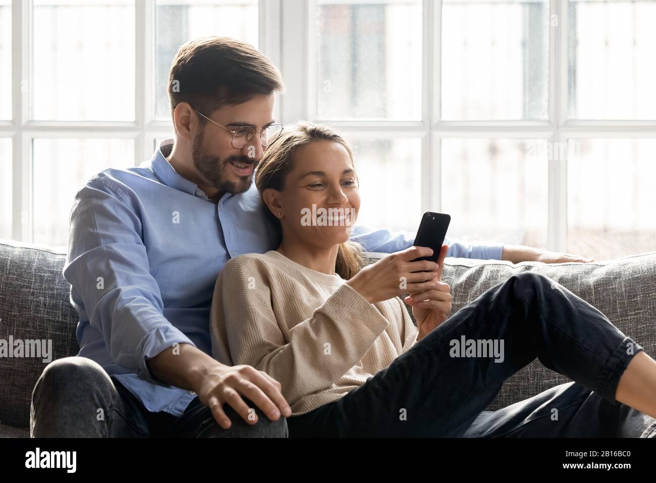 Coppia appoggiata sul divano divertirsi insieme online utilizzando lo smartphone Foto Stock