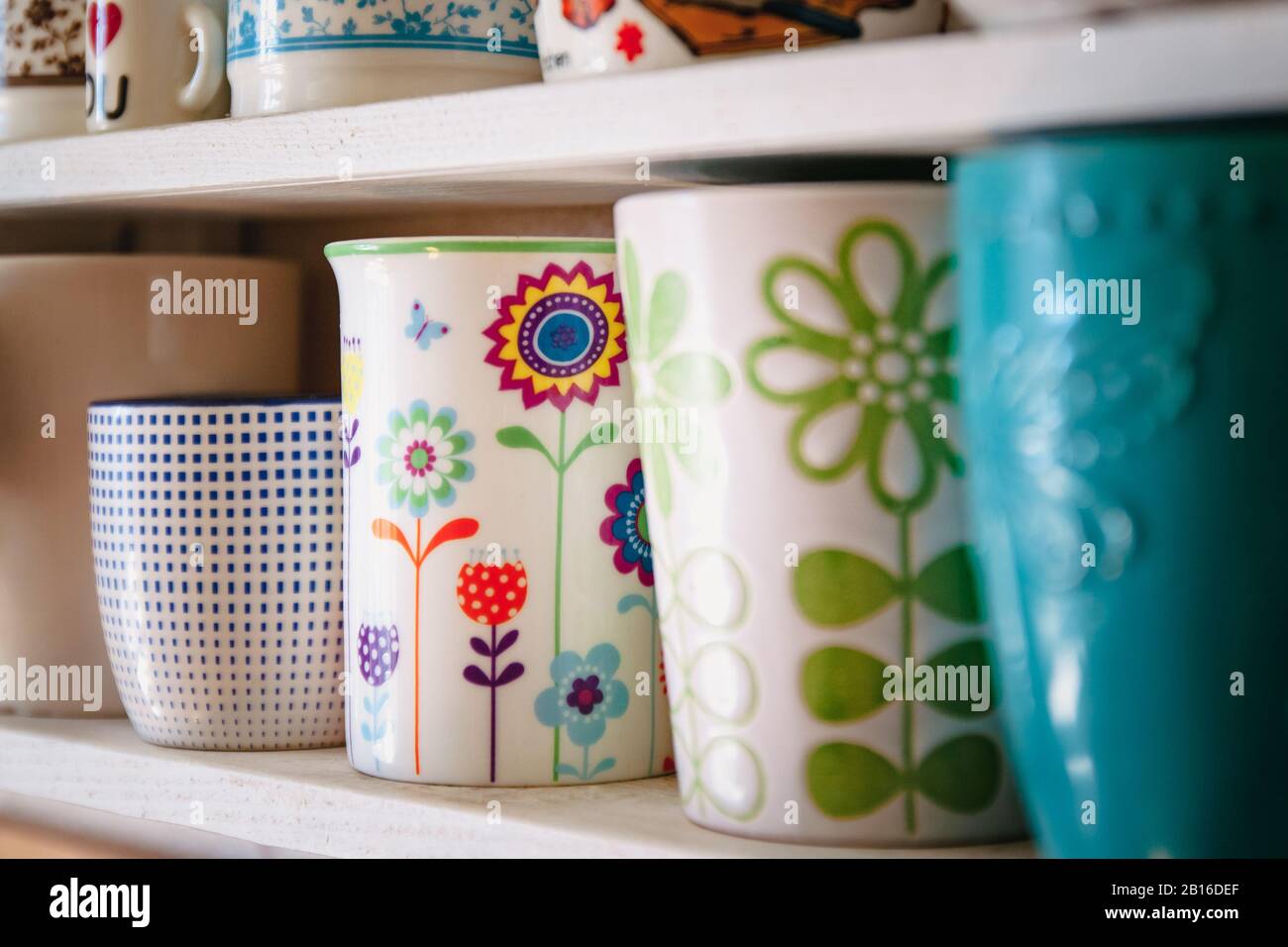 Una varietà di tazze e tazze in ceramica in primavera floreale luminoso stile stand in una fila su uno scaffale bianco casa. Foto Stock