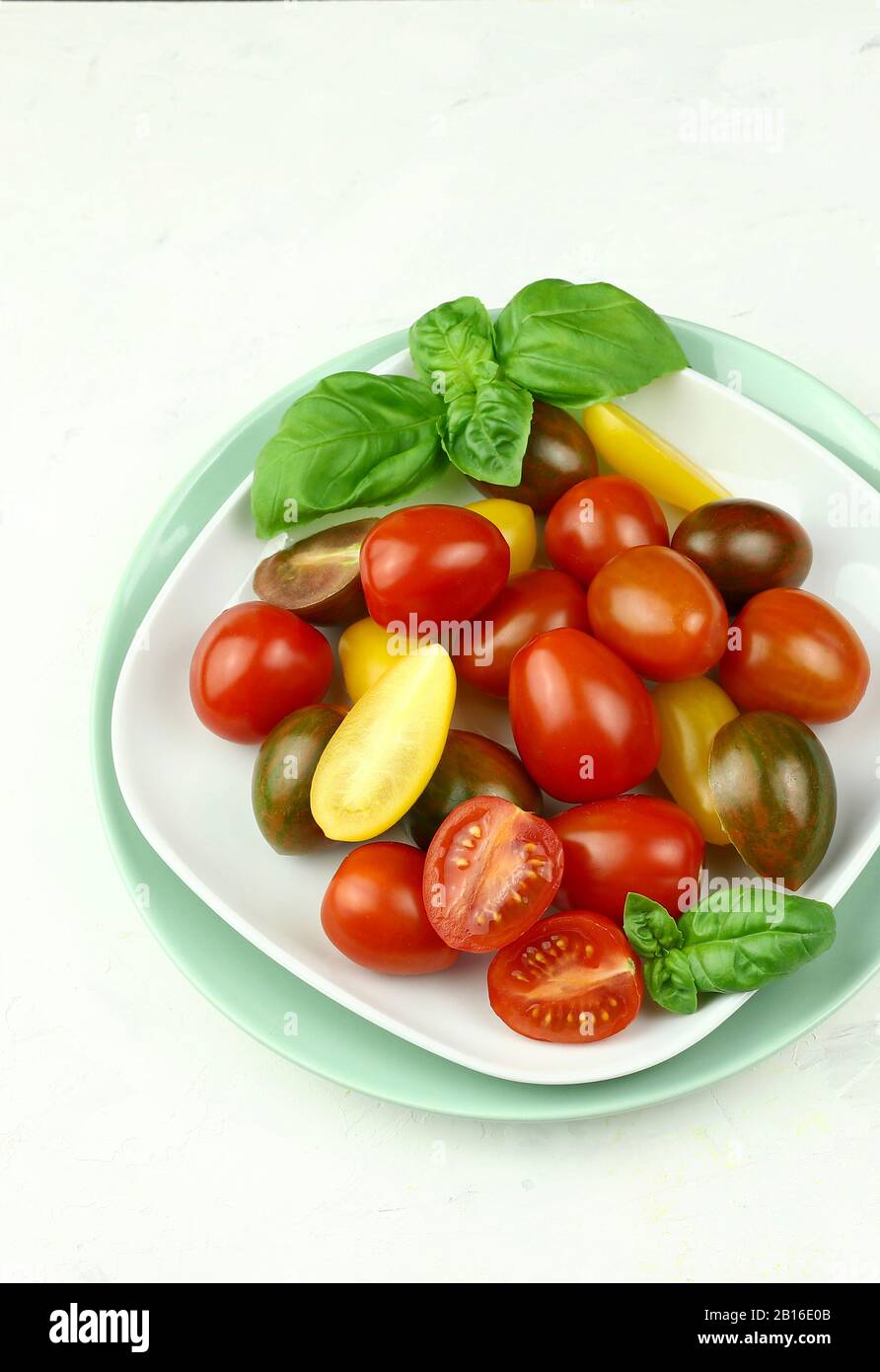 Layout creativo fatto di pomodori freschi colorati e basilico fresco. Concetto di cibo. Verdure isolate su sfondo bianco. Foto Stock
