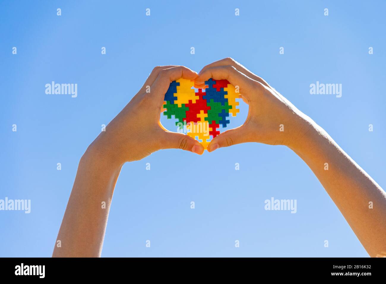 Mano del bambino che tiene il cuore colorato sullo sfondo blu del cielo. Mondo autismo concetto di giorno di consapevolezza Foto Stock
