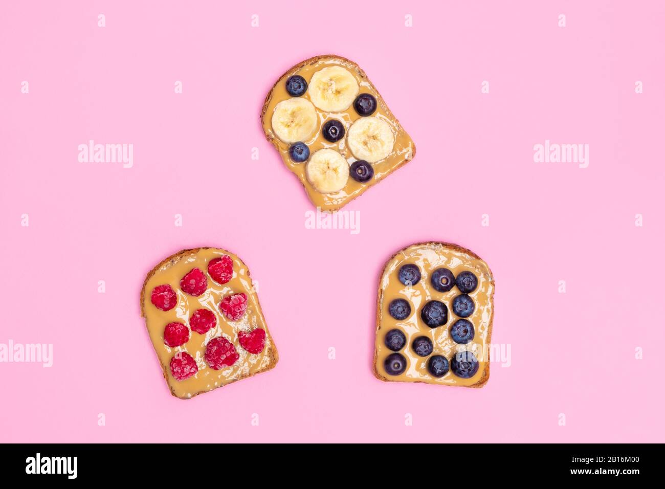 Direttamente sopra la vista del burro di arachide tostate con bacche e banana su sfondo rosa pastello, piatto Foto Stock