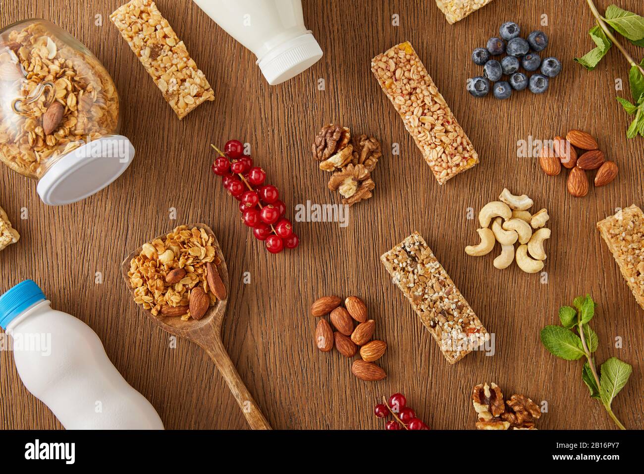 Vista dall'alto della composizione alimentare di frutti di bosco, noci, barrette di cereali e bottiglie di yogurt e latte su sfondo di legno Foto Stock