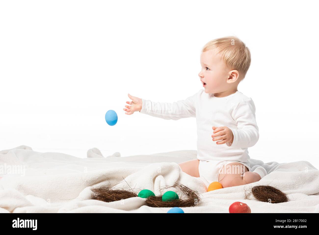 Bambino che lancia l'uovo di pasqua mentre si siede su coperta isolata su bianco Foto Stock