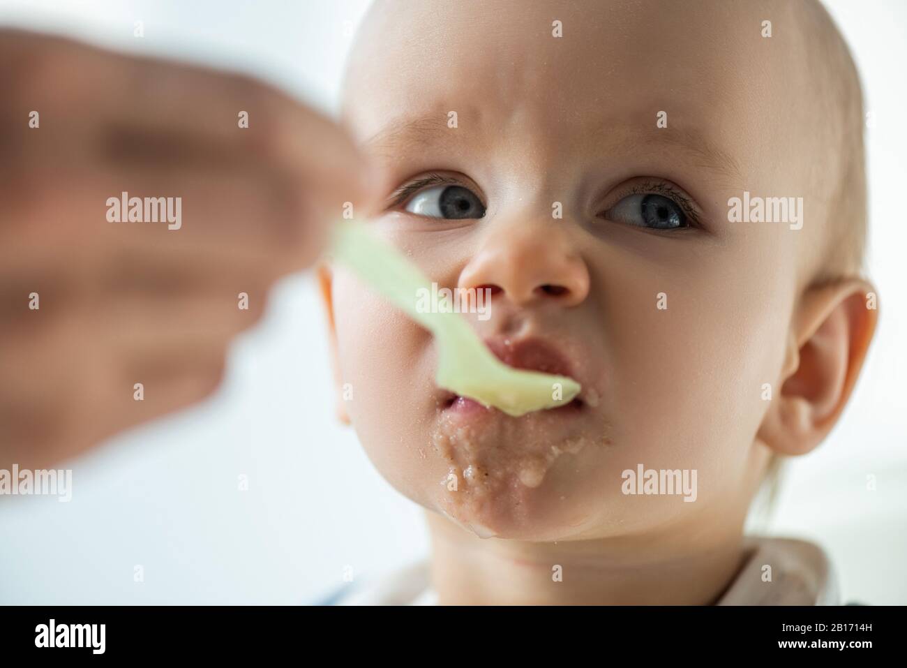 Fuoco selettivo della madre che alimenta il bambino con purea sullo sfondo grigio Foto Stock