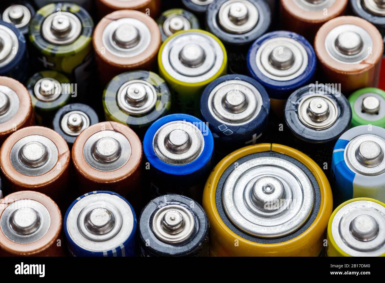 Primo piano delle estremità positive delle batterie colorate scaricate di diverse dimensioni e formati, vista dall'alto, messa a fuoco selettiva. Batteria alcalina usata. Hazardou Foto Stock