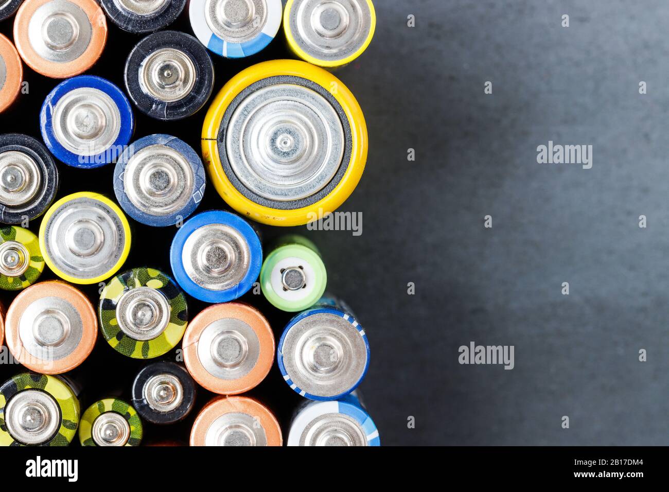Primo piano delle estremità positive delle batterie colorate scaricate di diverse dimensioni e formati, vista dall'alto, spazio di copia. Batteria alcalina usata su retro nero Foto Stock