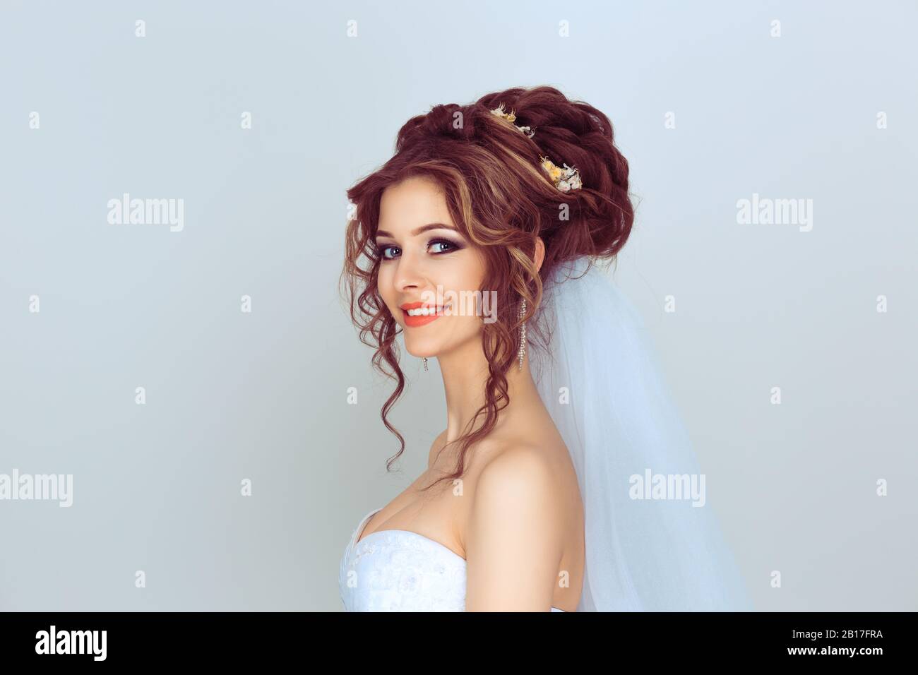 Sposo nel profilo che guarda la macchina fotografica sorridente. Ritratto di una bella ragazza con fiori sui capelli in abito da sposa isolato su sfondo azzurro Foto Stock