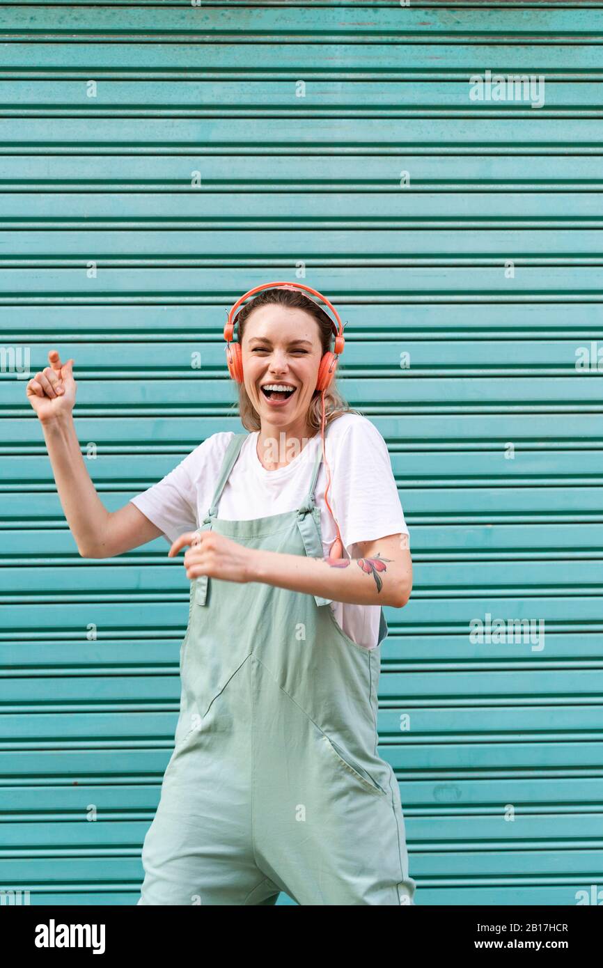 Donna che ride ascoltando musica davanti al serranda blu Foto Stock