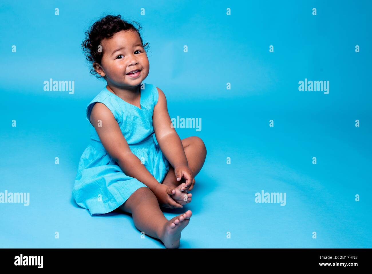 Ritratto di bambina a piedi nudi vestita di blu chiaro su sfondo blu Foto Stock