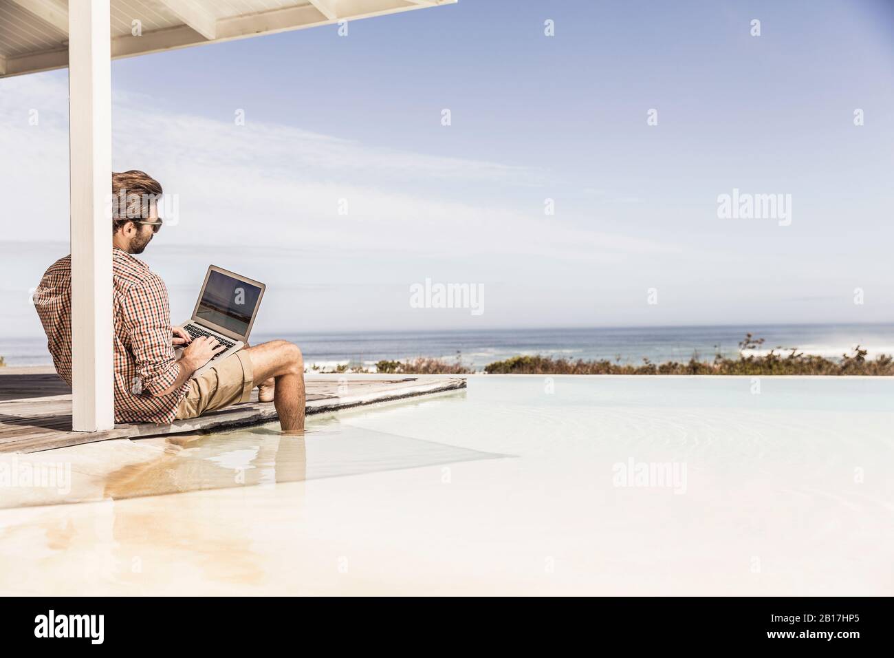 Uomo che lavora su un computer portatile accanto alla piscina in una casa sulla spiaggia Foto Stock