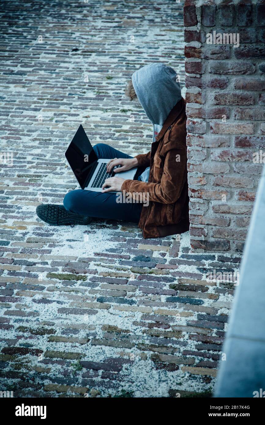 Adolescente che usa il laptop e seduto su un pavimento in pietra in città Foto Stock