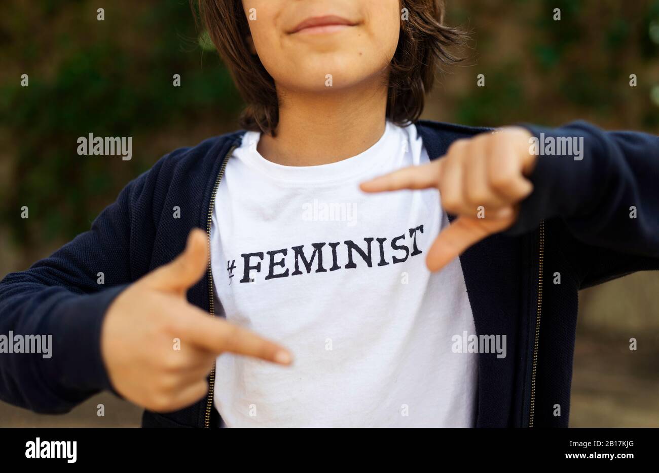 Ragazzo in piedi per strada con stampa su t-shirt, dicendo Femminista, facendo cornice dito Foto Stock