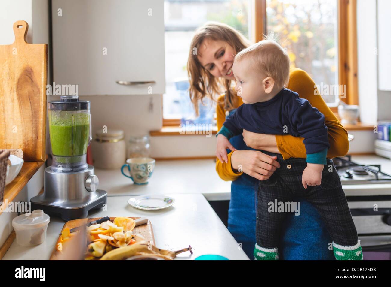 Donna in cucina che prepara frullato sano e tiene il suo figlio del bambino Foto Stock