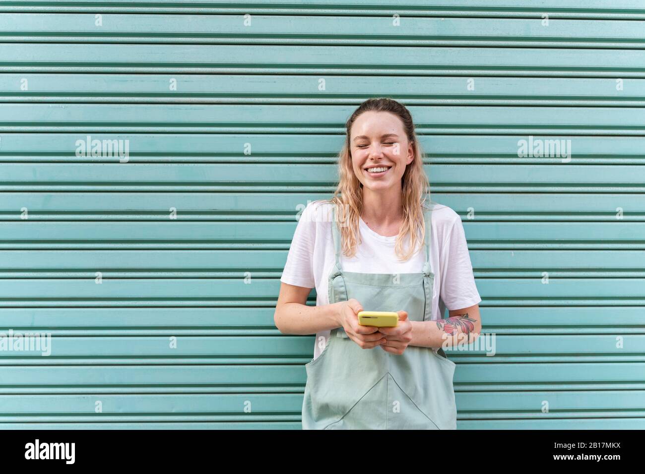 Giovane donna che ride utilizzando lo smartphone davanti al serranda blu Foto Stock