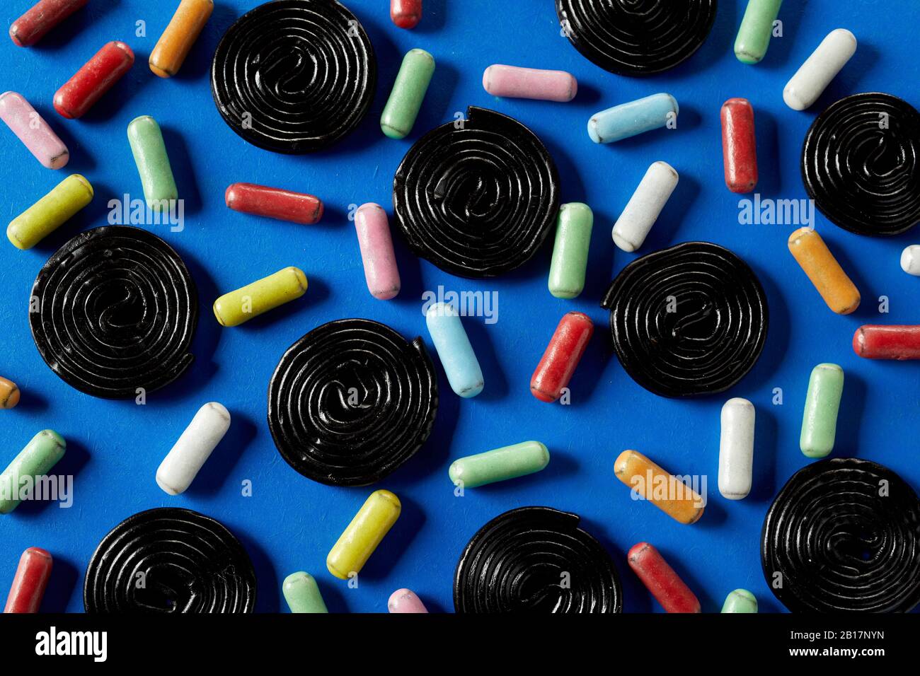 Ruote a spirale di caramella di liquirizia su blu inframmezzato con zucchero di liquirizia rivestito nei colori dell'arcobaleno Foto Stock