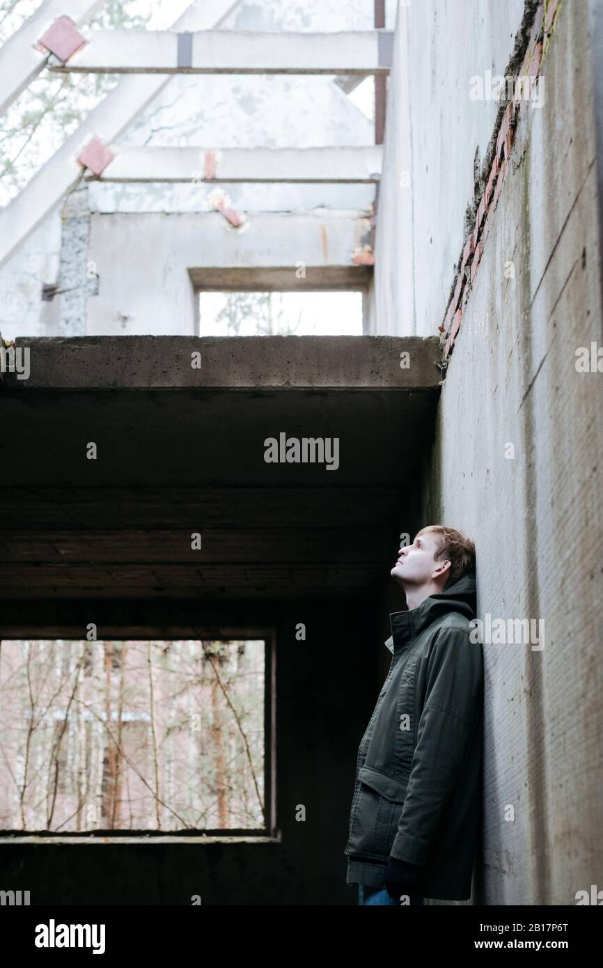 Uomo appoggiato a muro di cemento di una rovina che guarda in su Foto Stock