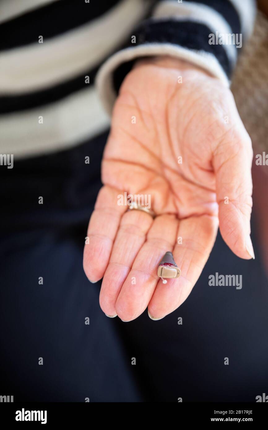 Mano di donna anziana con moderno apparecchio acustico Foto Stock