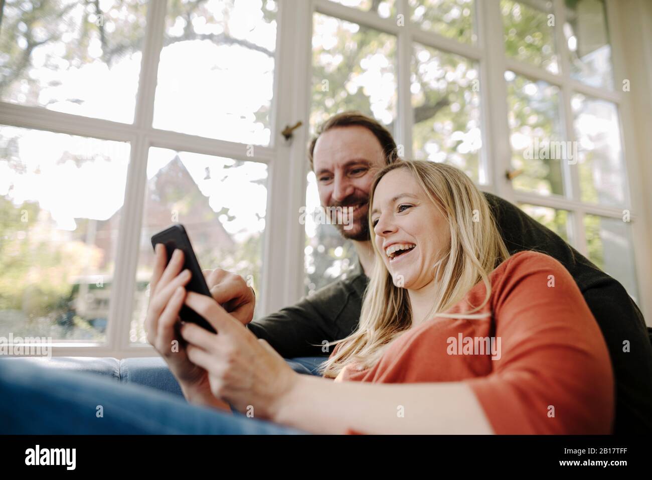 Ridere coppia utilizzando lo smartphone a casa Foto Stock