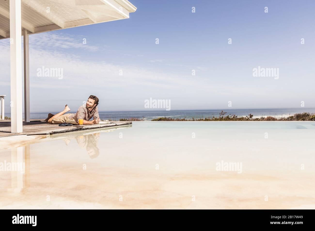 Uomo che giace accanto alla piscina in una casa sulla spiaggia Foto Stock
