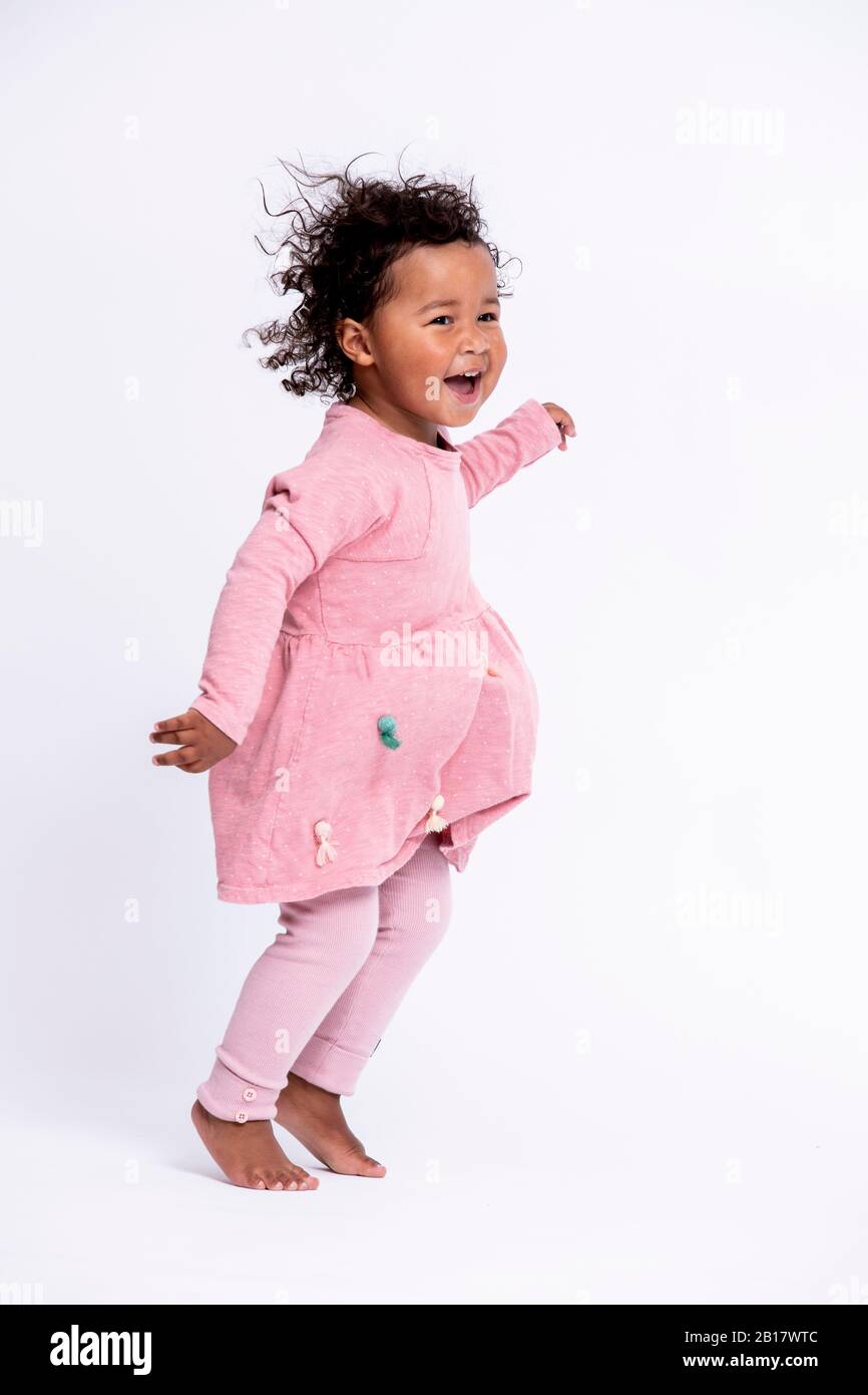 Ritratto di bambina a piedi nudi vestita con un salto rosa davanti a sfondo bianco Foto Stock