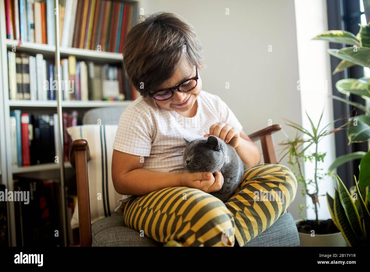 Ragazzo sorridente seduto su poltrona solletico gatto Foto Stock