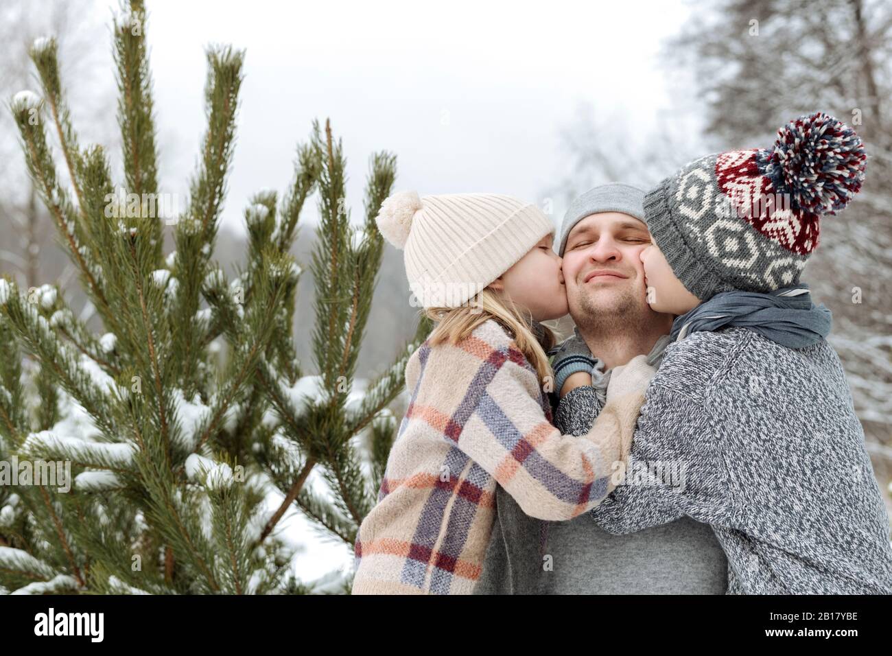Due bambini baciano il loro padre felice ad un abete in inverno Foto Stock