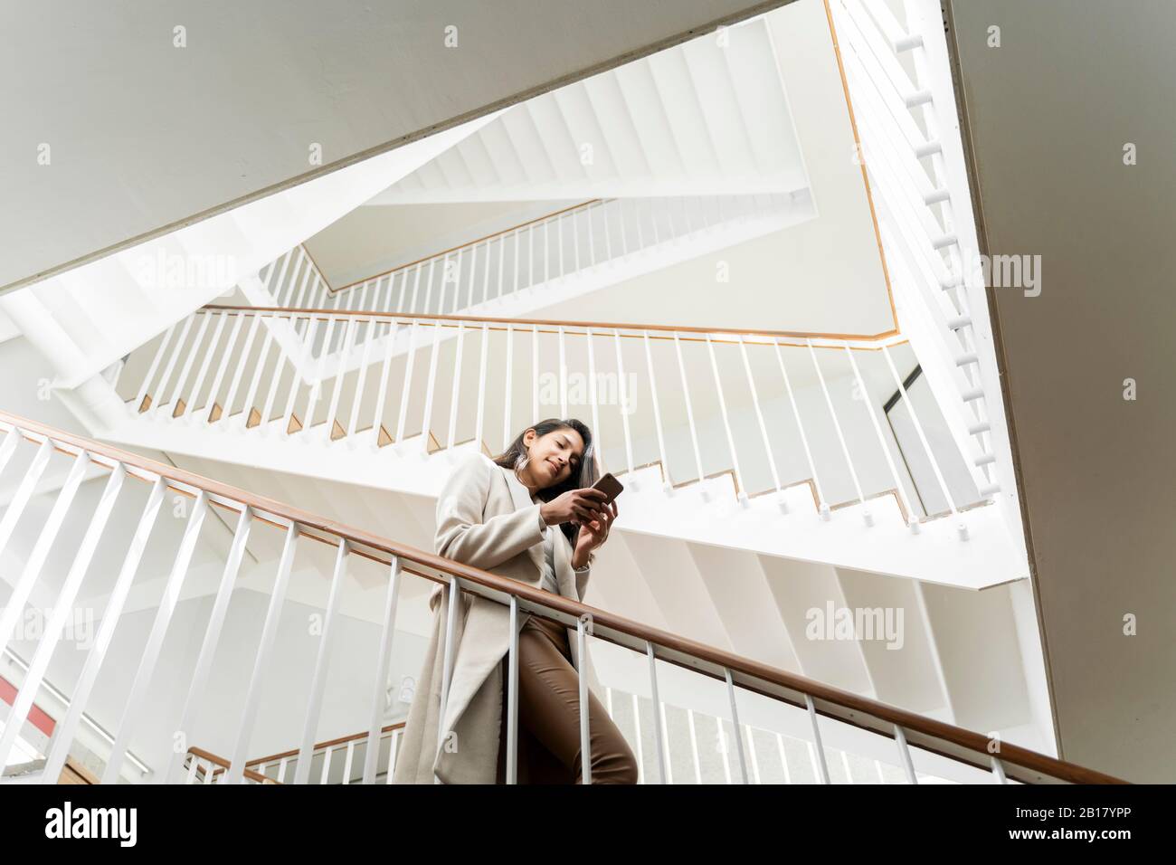 Giovane donna con smartphone che scende le scale in scala Foto Stock