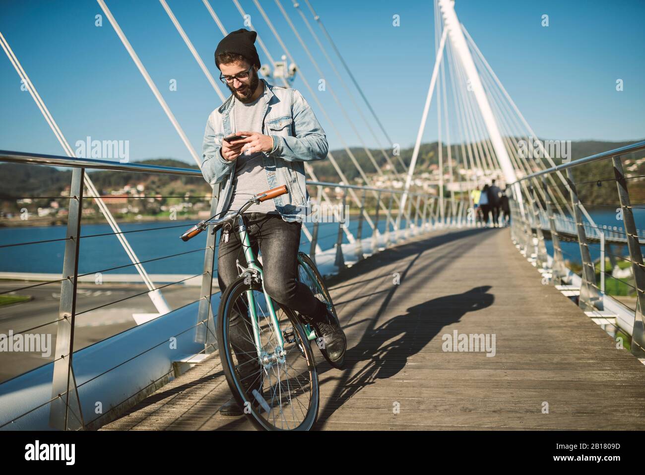 Giovane uomo che si trova in città con la sua bici da fixie, utilizzando lo smartphone Foto Stock