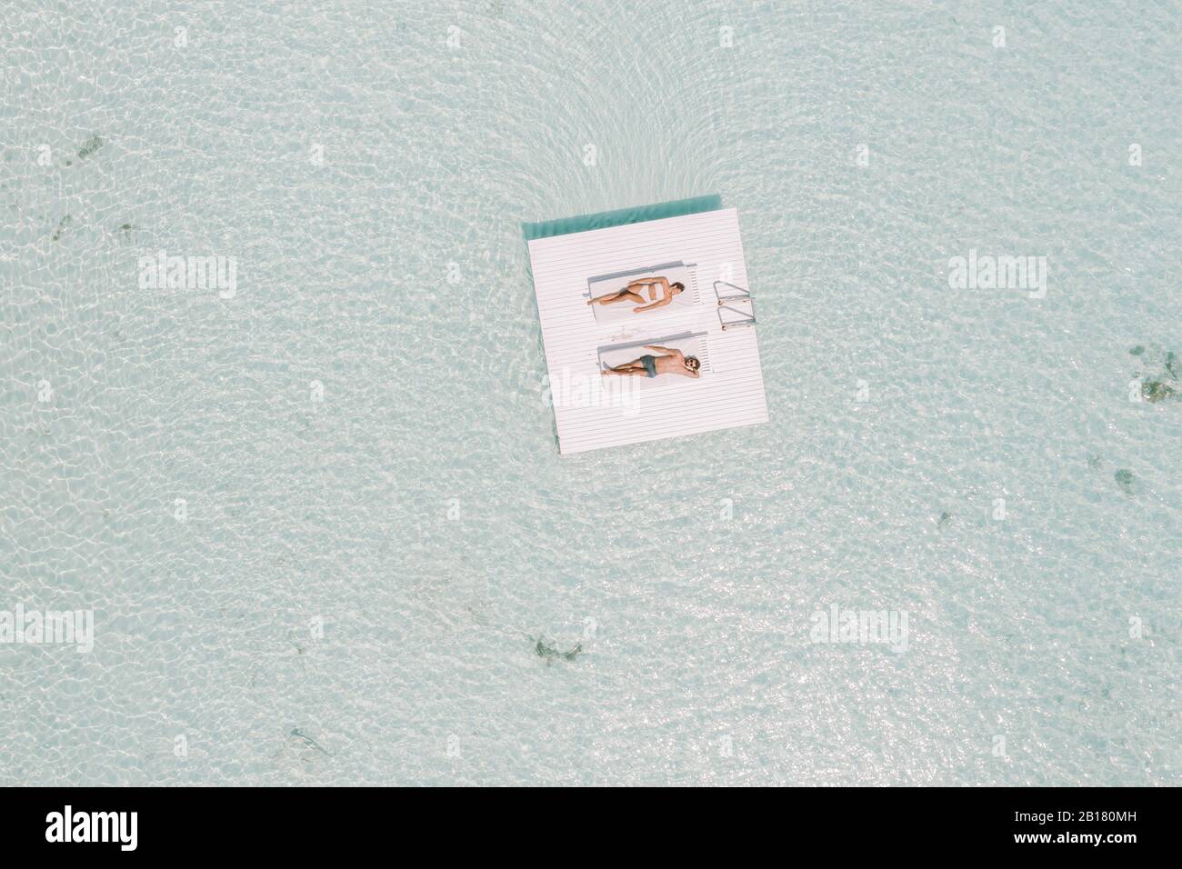 Coppia sdraiata su una piattaforma nel mare, Isola di Maguhdhuvaa, Atollo di Gaafu Dhalu, Maldive Foto Stock