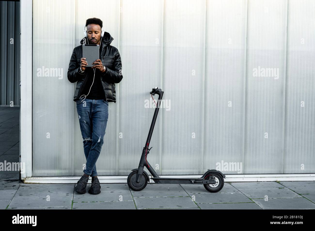 Uomo con cuffie, tablet e scooter elettrico all'aperto Foto Stock