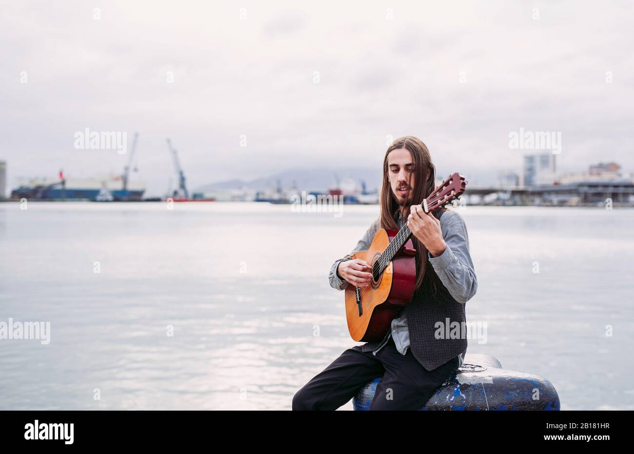 Giovane musicista che suona la chitarra al porto Foto Stock