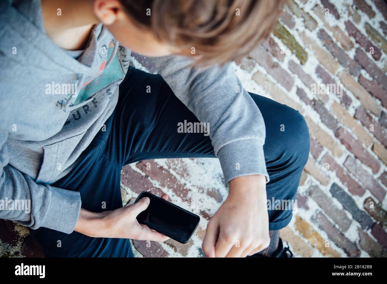 Adolescente che usa lo smartphone, seduto su un pavimento in pietra Foto Stock