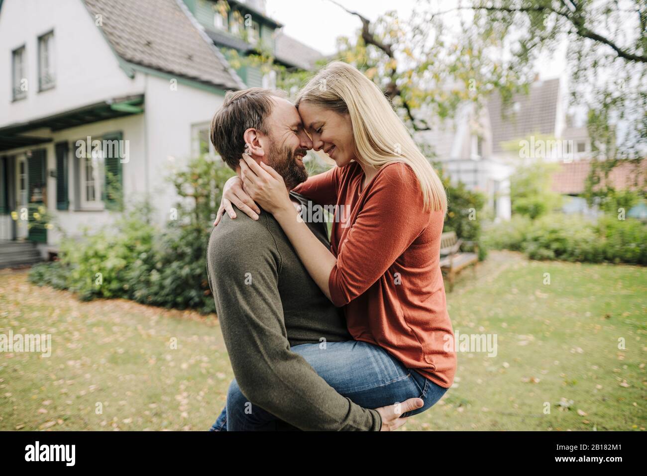 Felice coppia baciare in giardino, di fronte alla loro casa da sogno Foto Stock