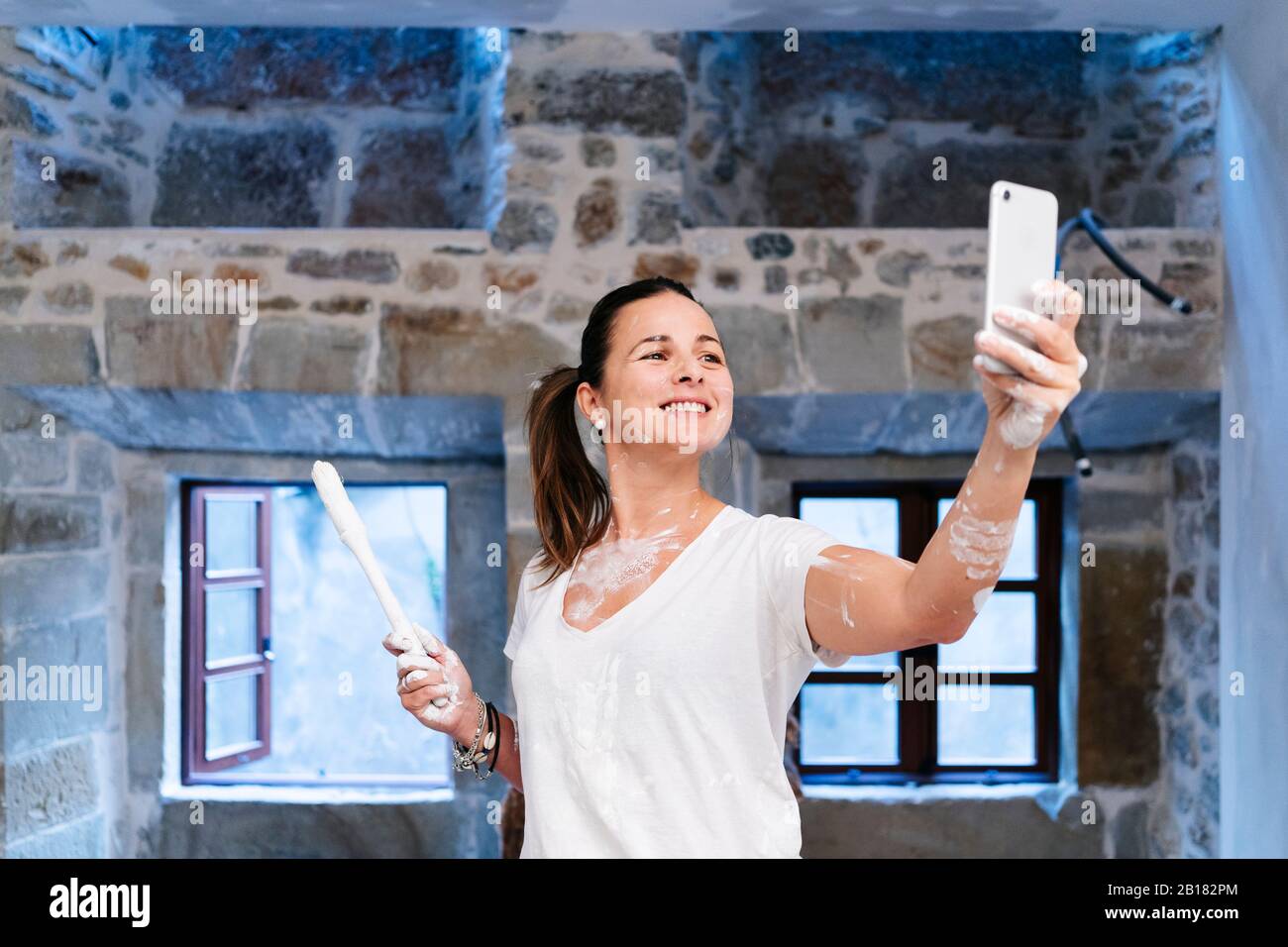 Donna che prende un selfie mentre dipinge le pareti della sua nuova casa Foto Stock