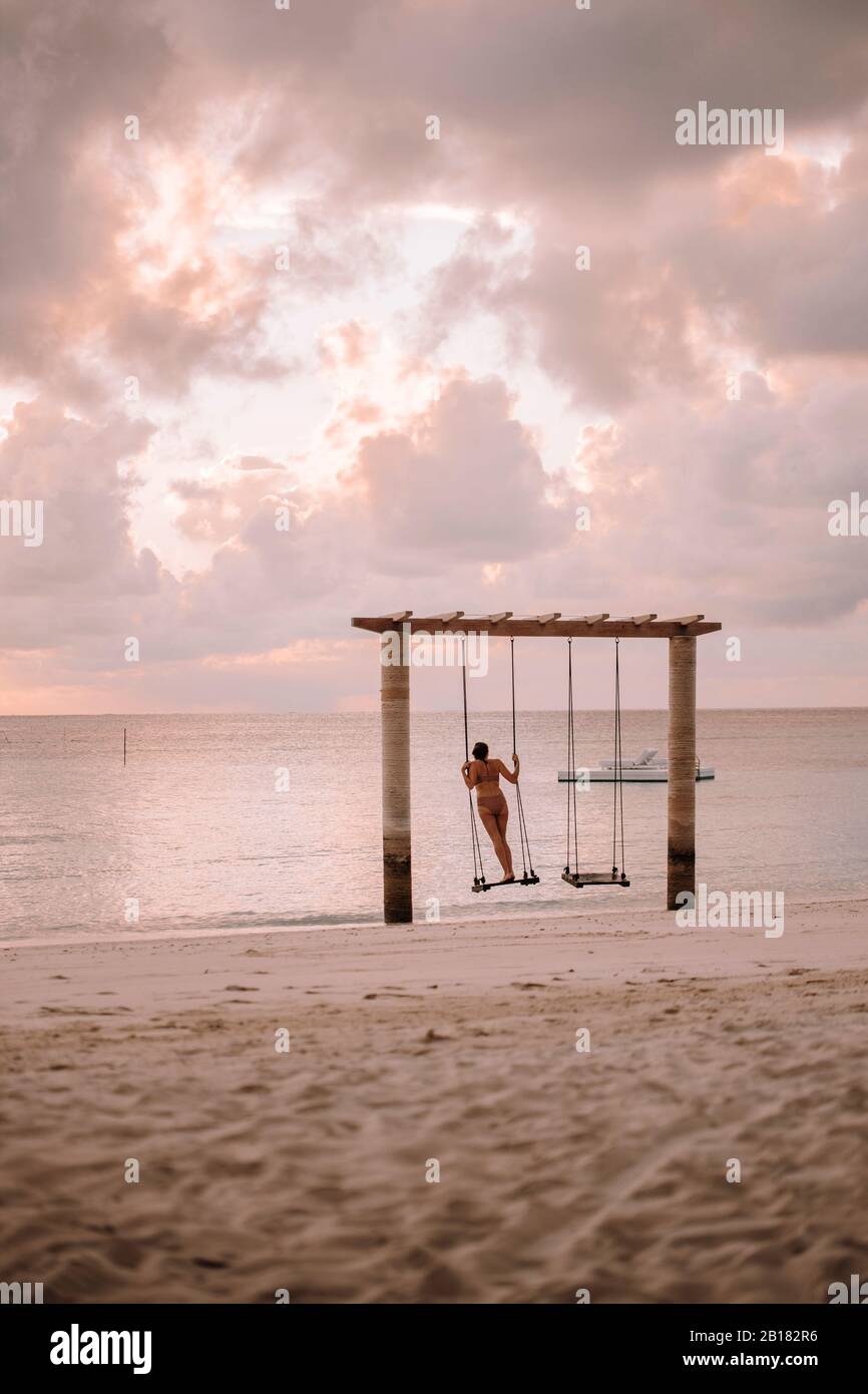 Donna in altalena al mare al tramonto, Isola di Maguhdhuvaa, Atollo di Gaafu Dhalu, Maldive Foto Stock