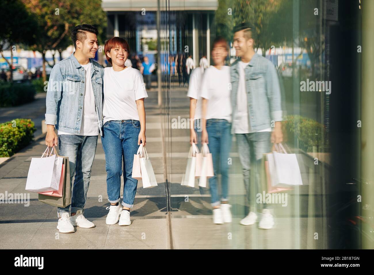 Sorridente giovane coppia asiatica a piedi in strada con borse di carta e guardando le vetrine negozio Foto Stock