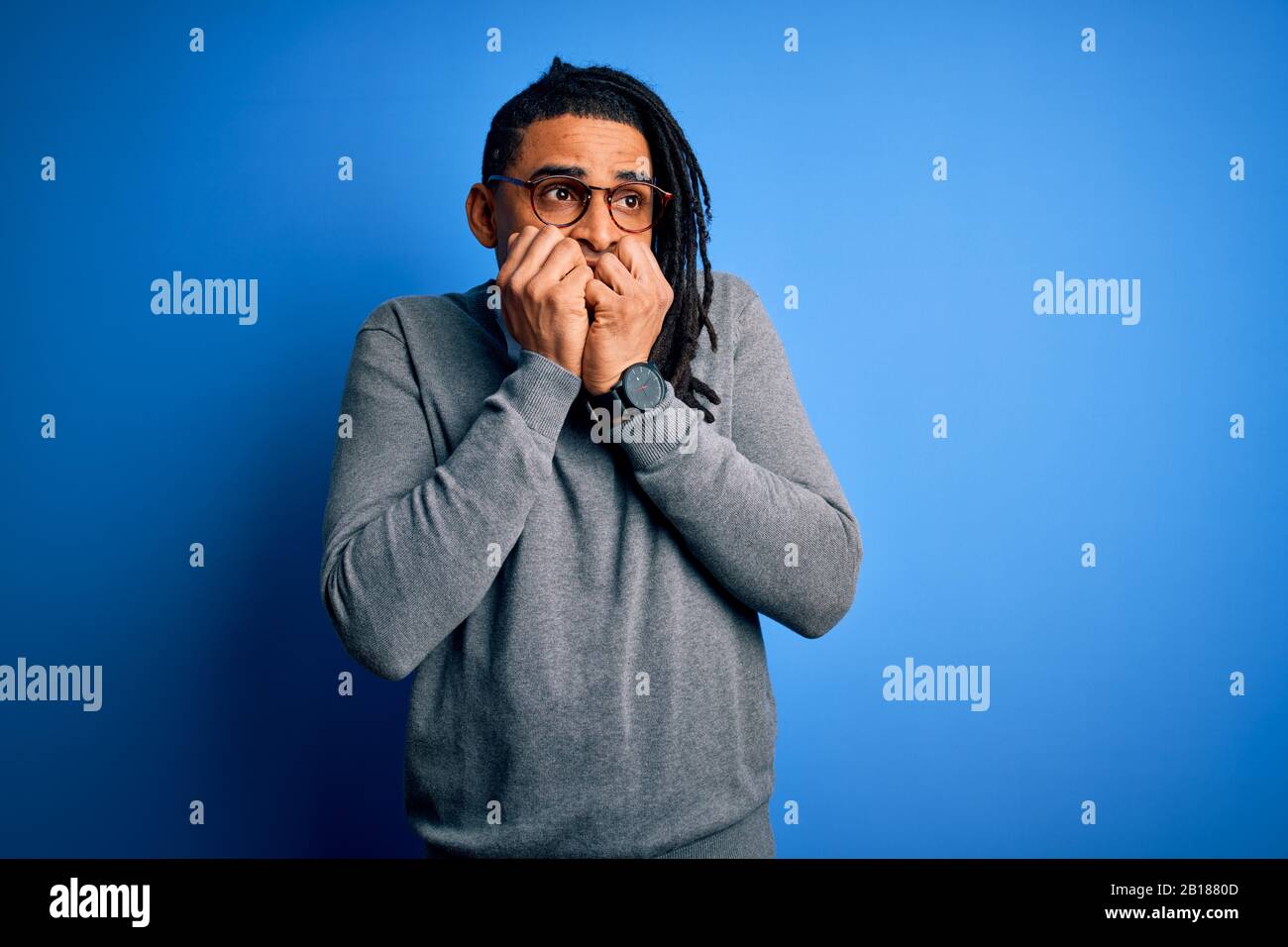 Giovane bell'uomo africano americano con temute serrature che indossano maglione casual e occhiali che guardano stressati e nervosi con le mani sulla bocca che mordono le unghie. Foto Stock