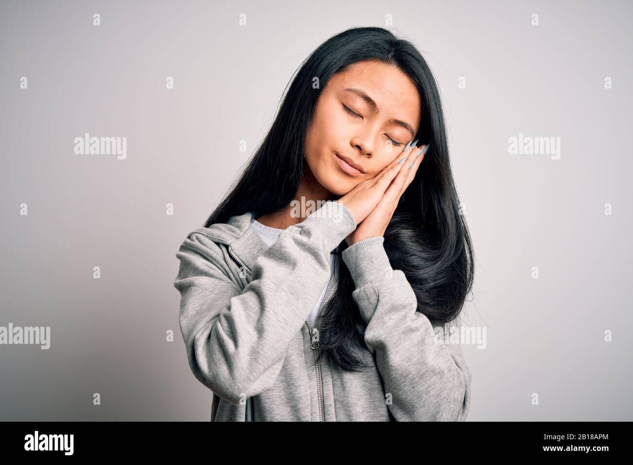 Giovane bella donna cinese sportiva indossando felpa su sfondo bianco isolato dormire stanco sognare e posare con le mani insieme mentre mq Foto Stock