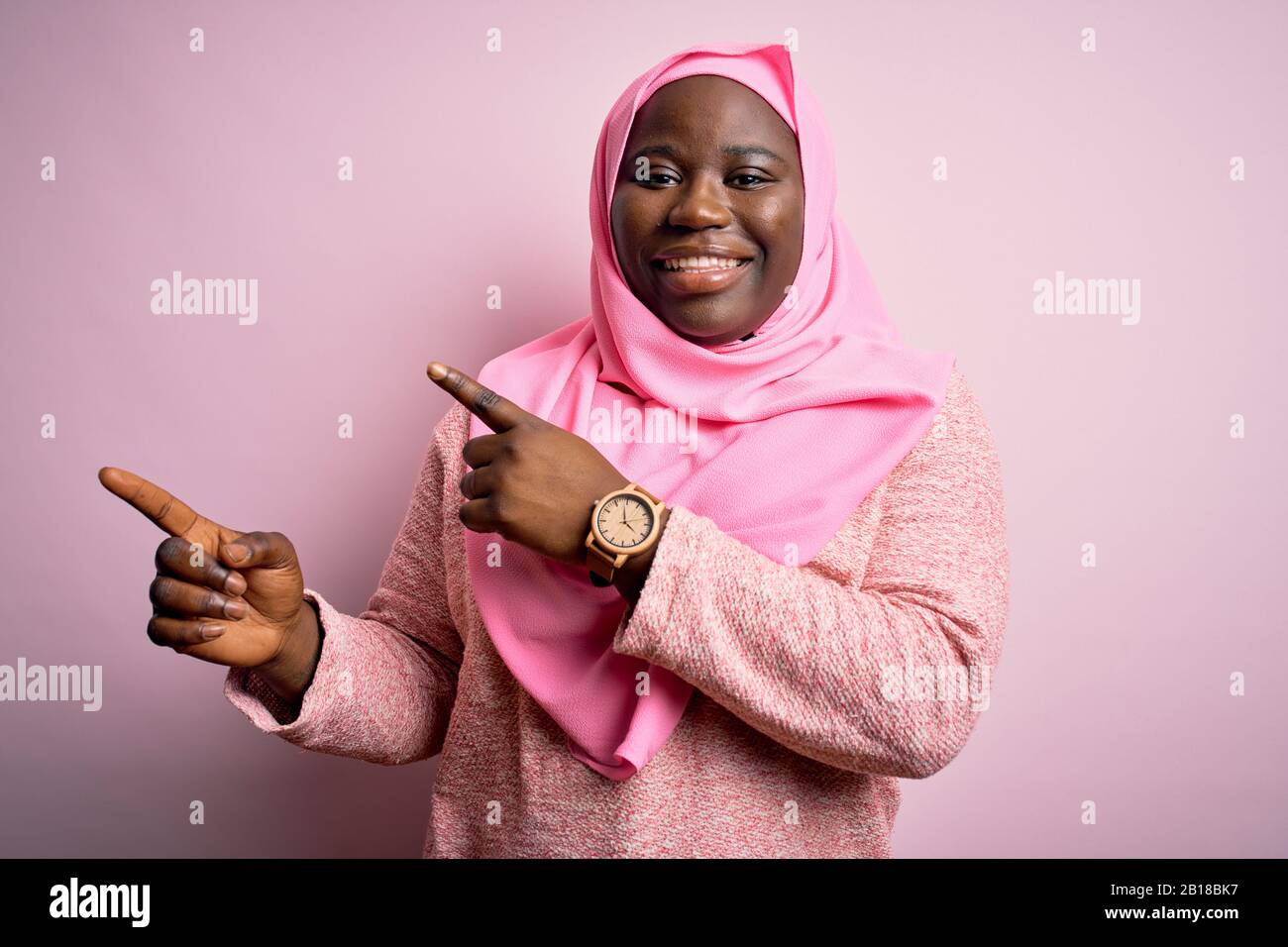 Giovane afroamericana più donna di taglia indossando hijab musulmano sopra sfondo rosa isolato sorridente e guardando la macchina fotografica che punta con due mani un Foto Stock