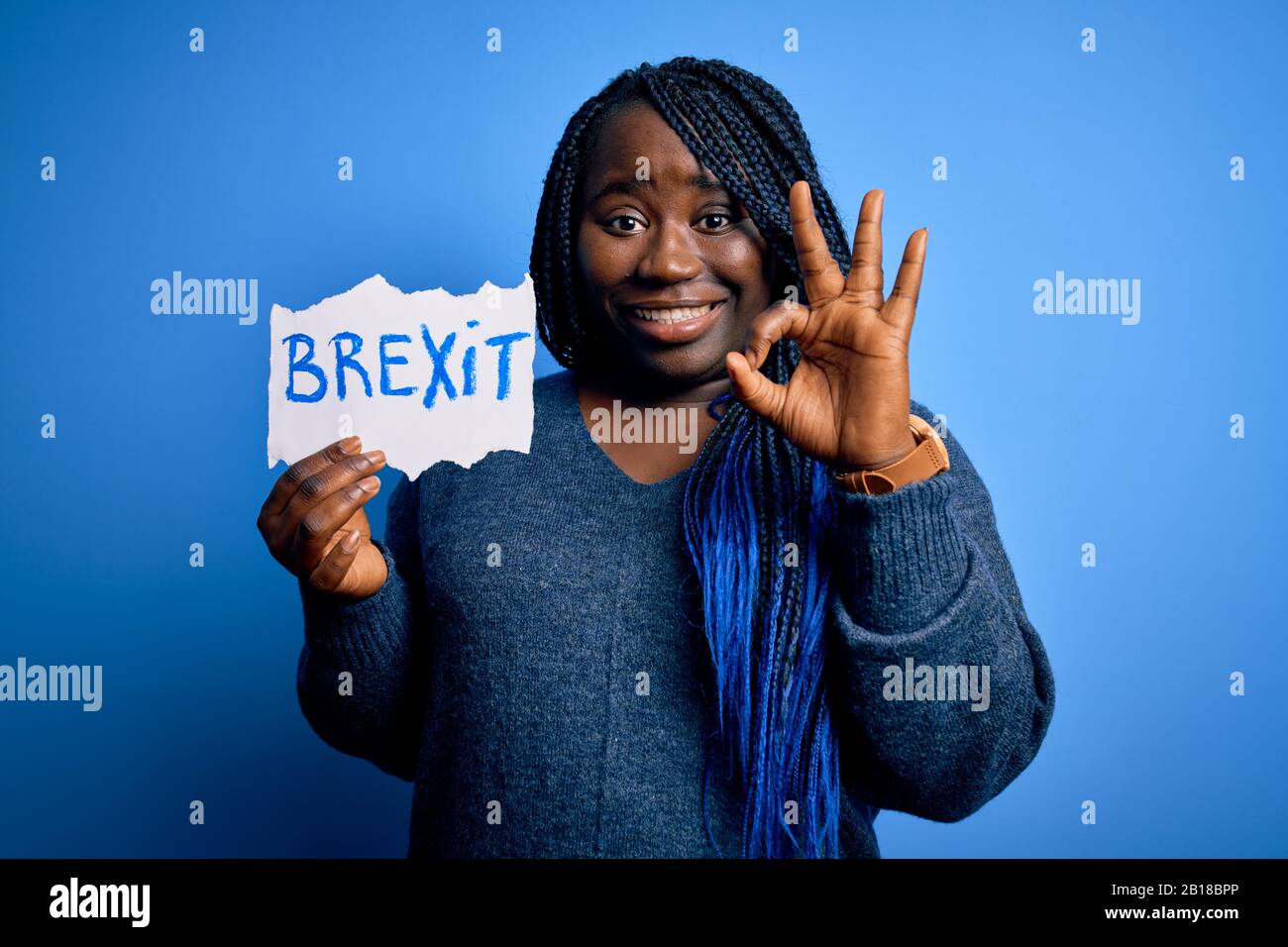 Giovane afroamericana più donna di taglia con trecce che tiene carta con il messaggio brexit facendo segno ok con le dita, simbolo eccellente Foto Stock