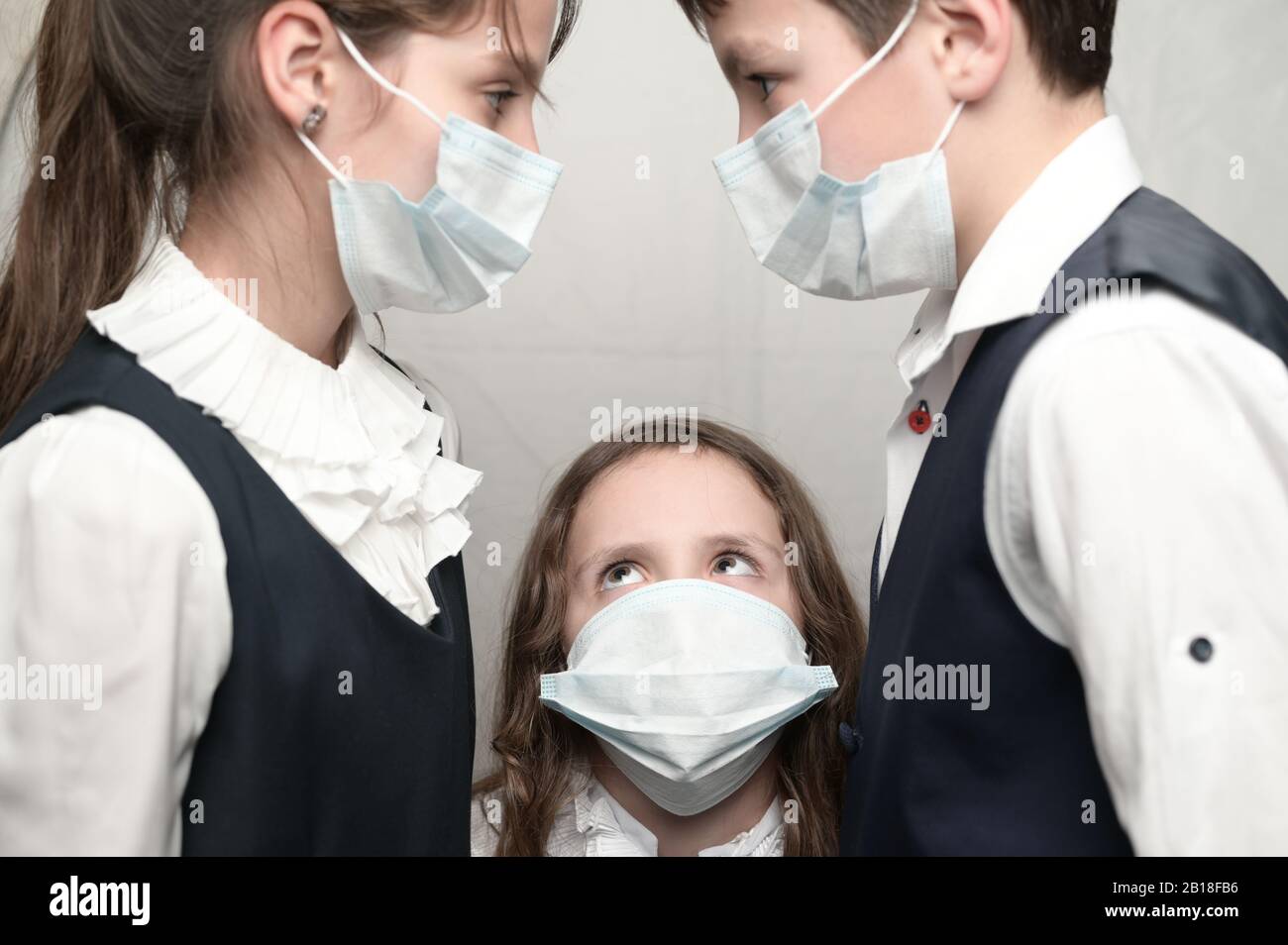Coronavirus COVID-19 2019-nIl concetto di focolaio di tre bambini malati in uniforme scolastica guardano l'uno all'altro Foto Stock