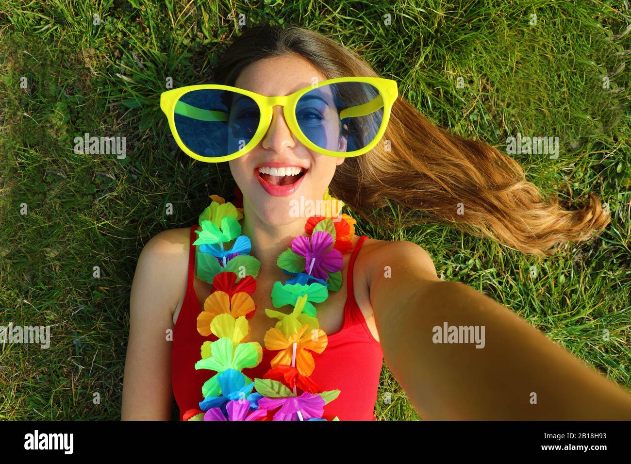 Ragazza prendere autoritratto dopo festa di Carnevale. Selfie di giovane  donna con grandi divertenti occhiali da sole e garland carnevale sdraiato  sull'erba Foto stock - Alamy